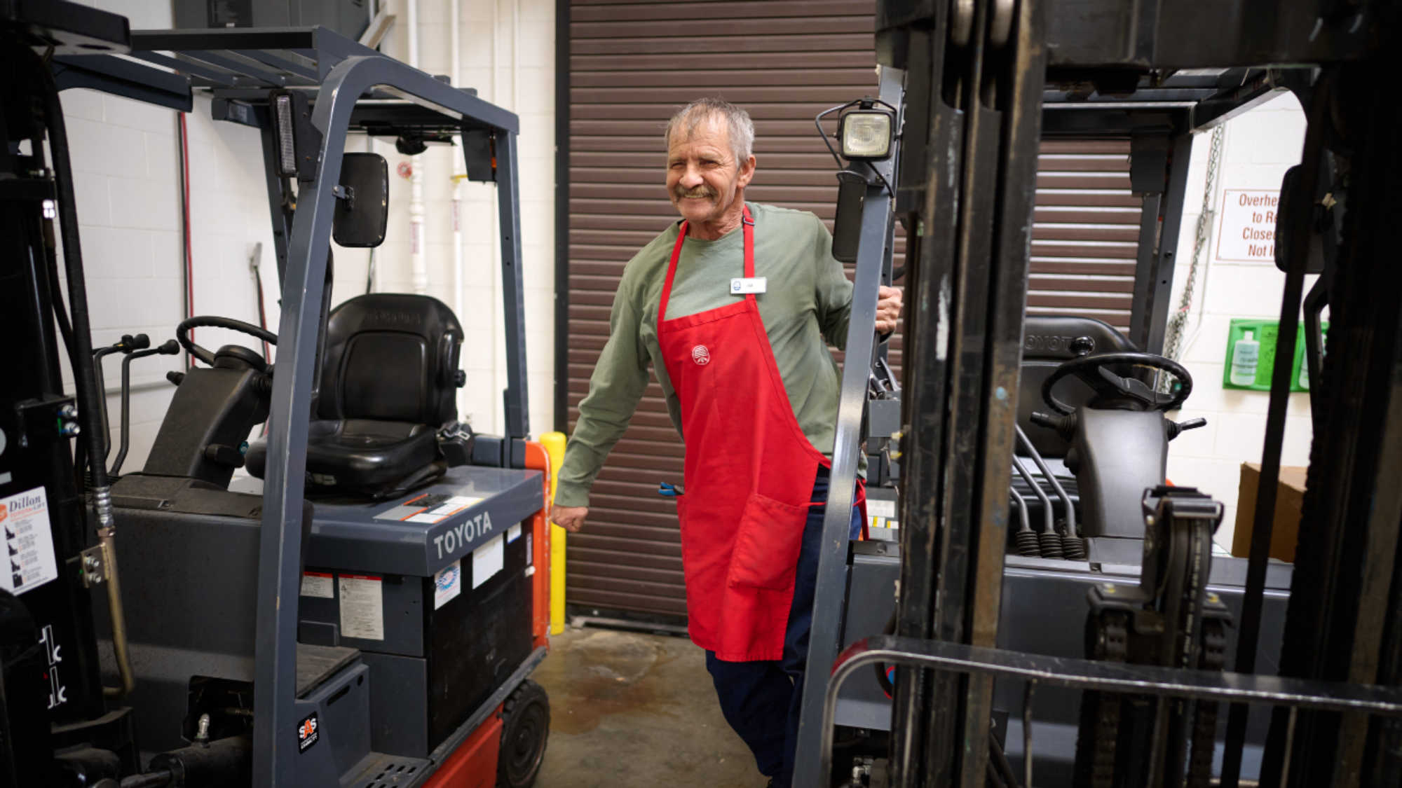 A male DI associate smiles as he steps down from a forklift.